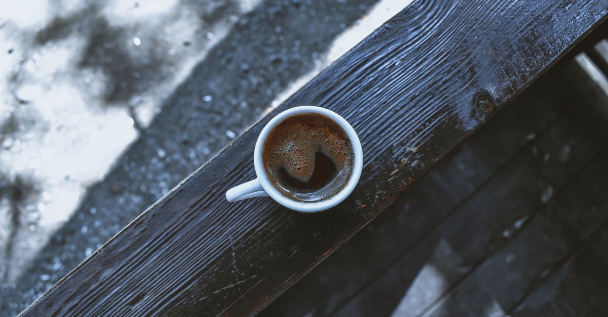 Taza de café sobre una mesa de madera junto a una bolsa de papel